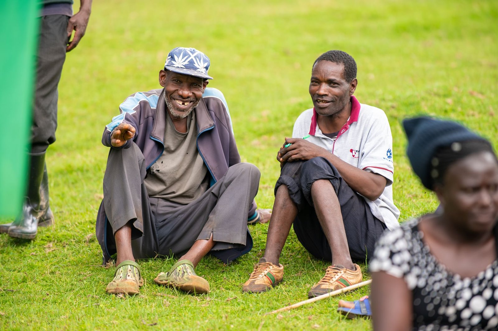 Two men sitting happily on grass in Eldoret, Kenya, enjoying a sunny day outdoors.
