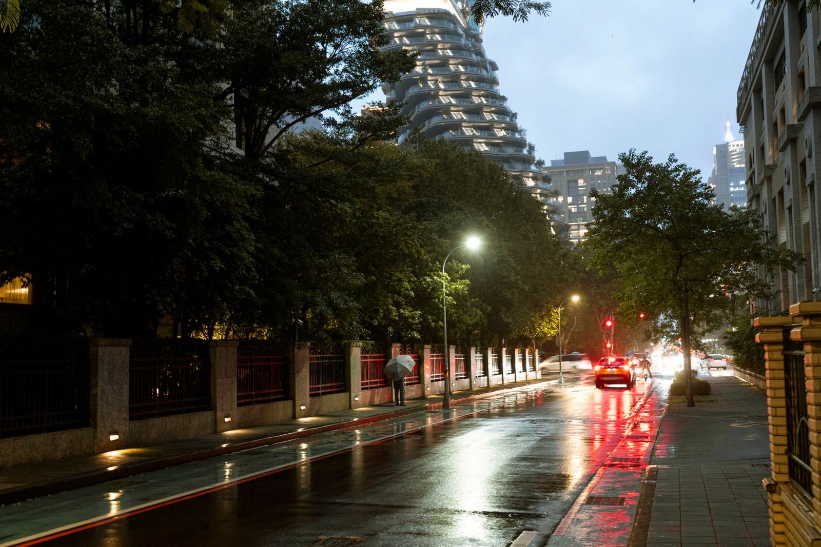 City street at dusk with wet pavement reflecting lights in a rainy urban setting.