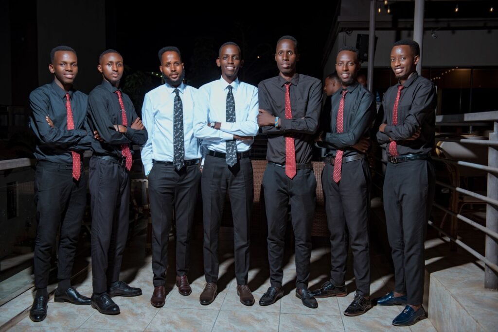 Seven men in formal attire posing confidently outdoors during a nighttime event.