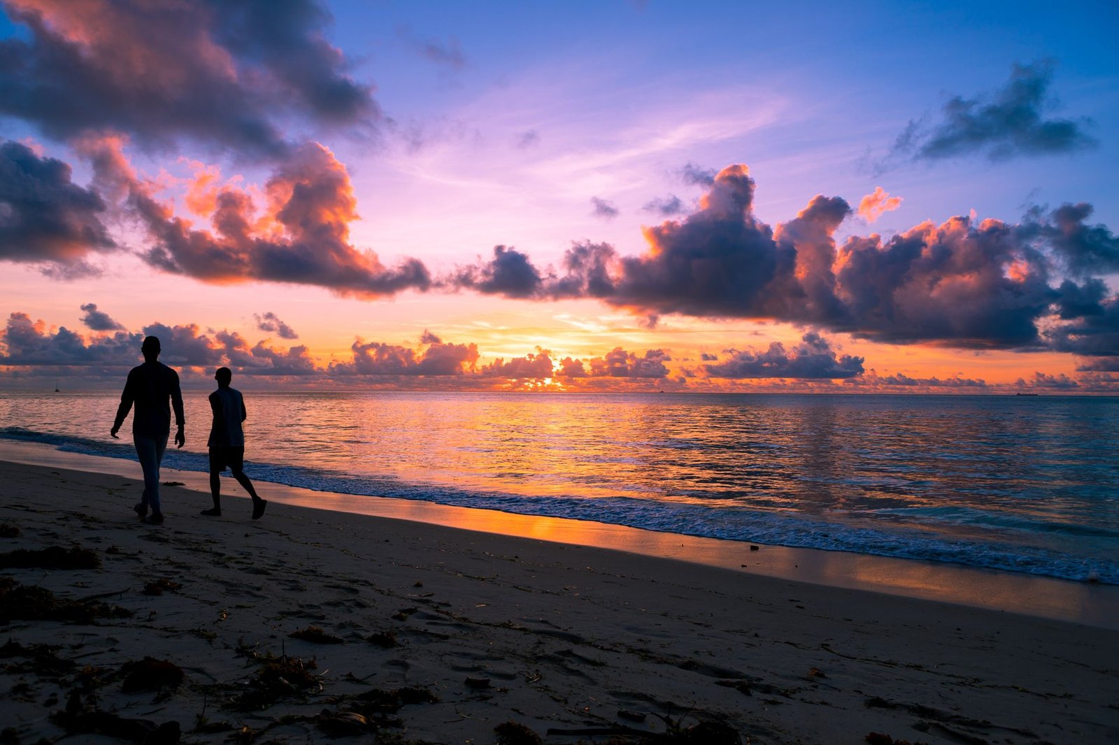Silhouettes strolling on Mombasa's serene beach at sunrise with vibrant sky colors.