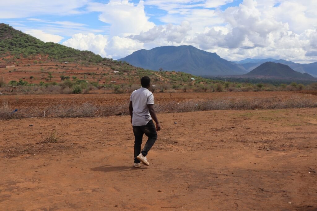 A man walks on the dry, scenic landscape of Taveta, Kenya with lush mountains.