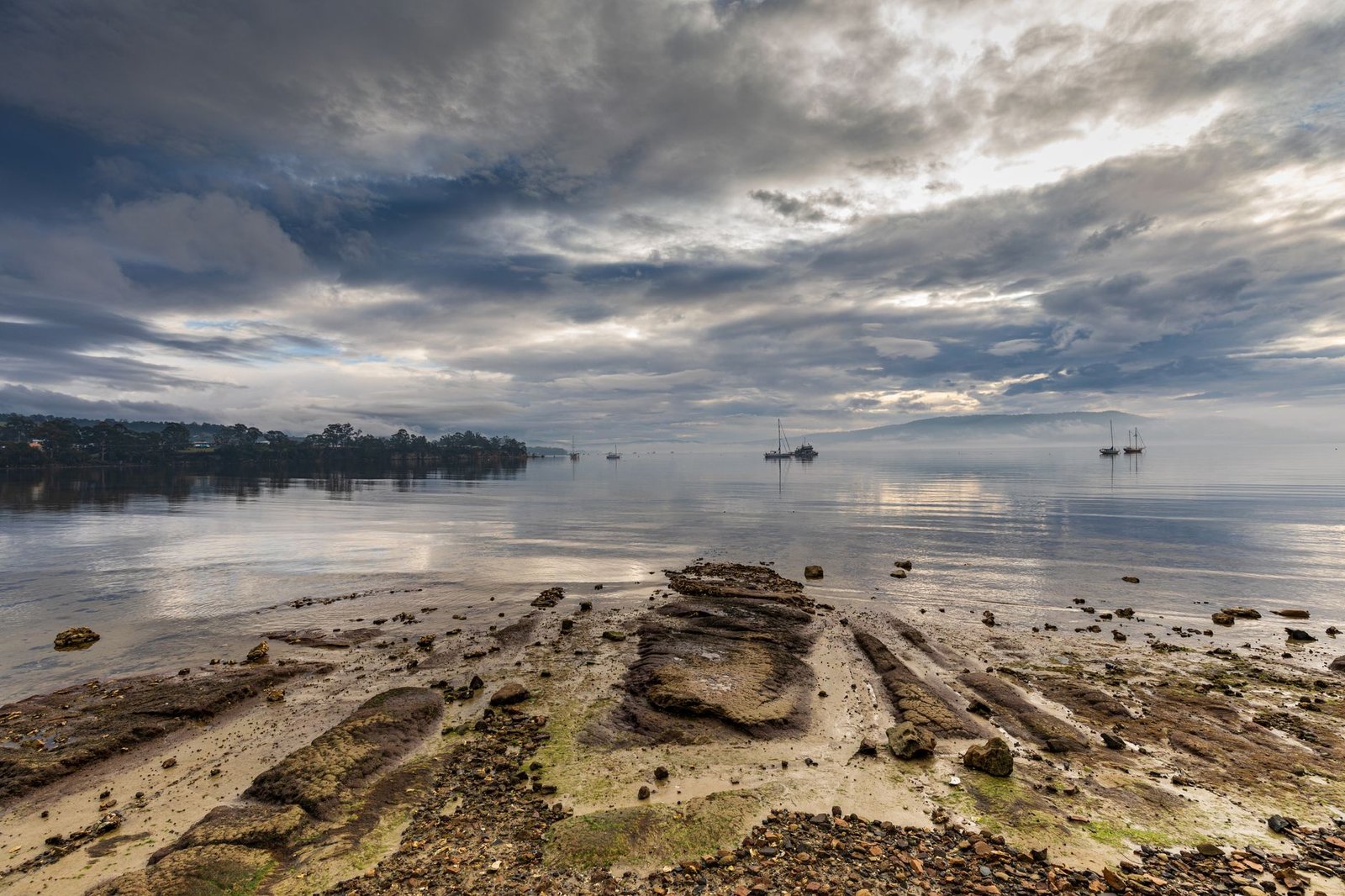 Tranquil view of Snug Beach in Tasmania with calm waters and moody skies under daylight.