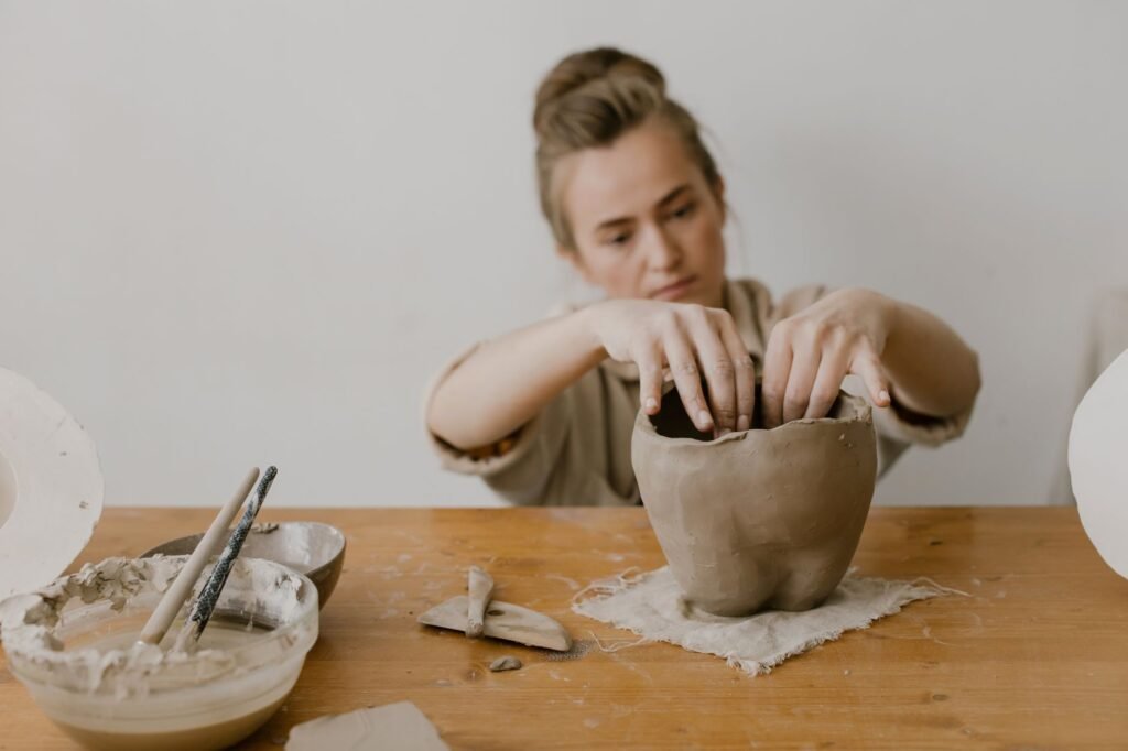 Focused artisan shaping clay pottery with hands in a workshop setting.