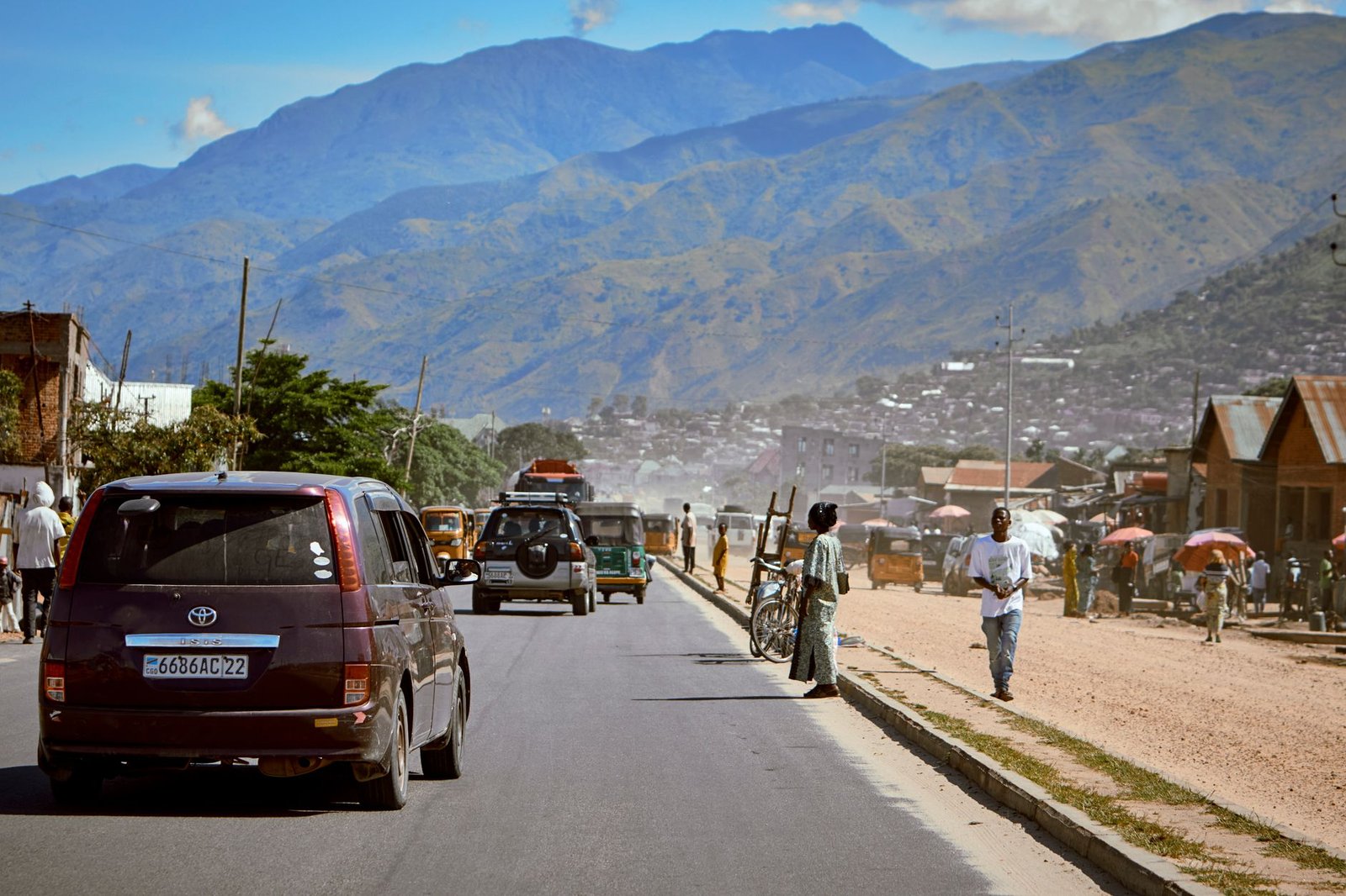 A busy street in an African town against a mountainous backdrop, showcasing local life.