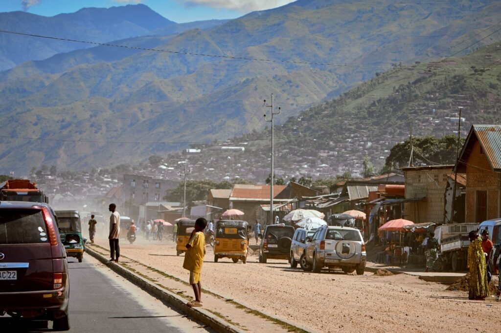 A vibrant rural street bustling with people and vehicles against a stunning mountain backdrop.