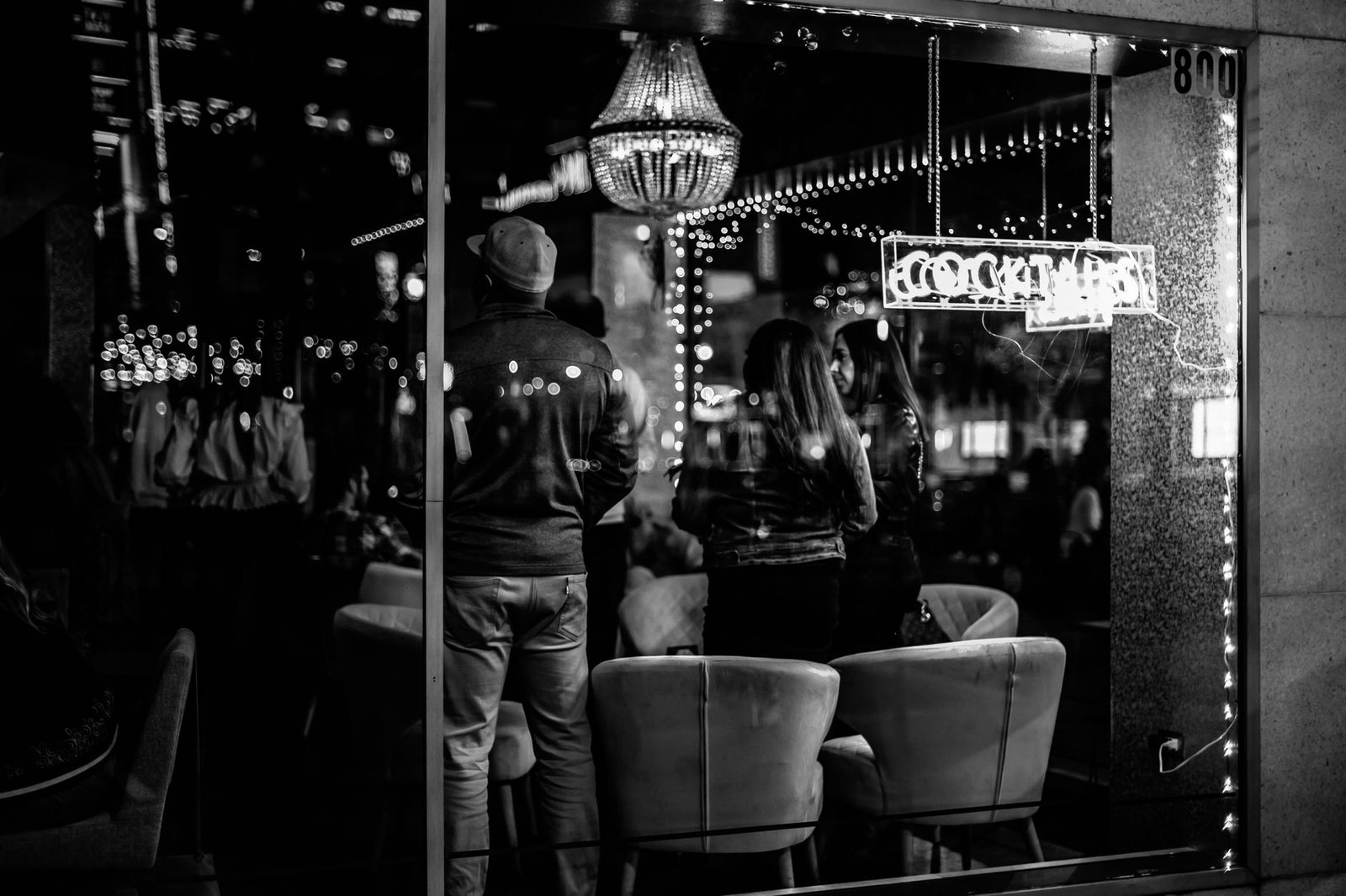 Black and white of young anonymous people spending time in bar with bright lights at night