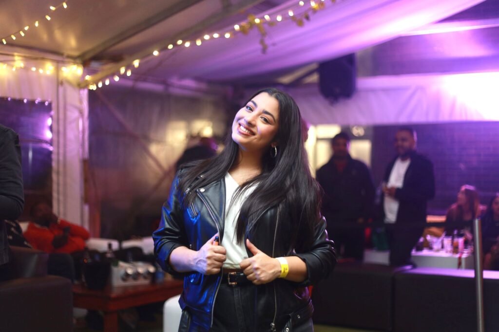Happy woman in a black leather jacket enjoying a festive indoor event with friends in South Africa.