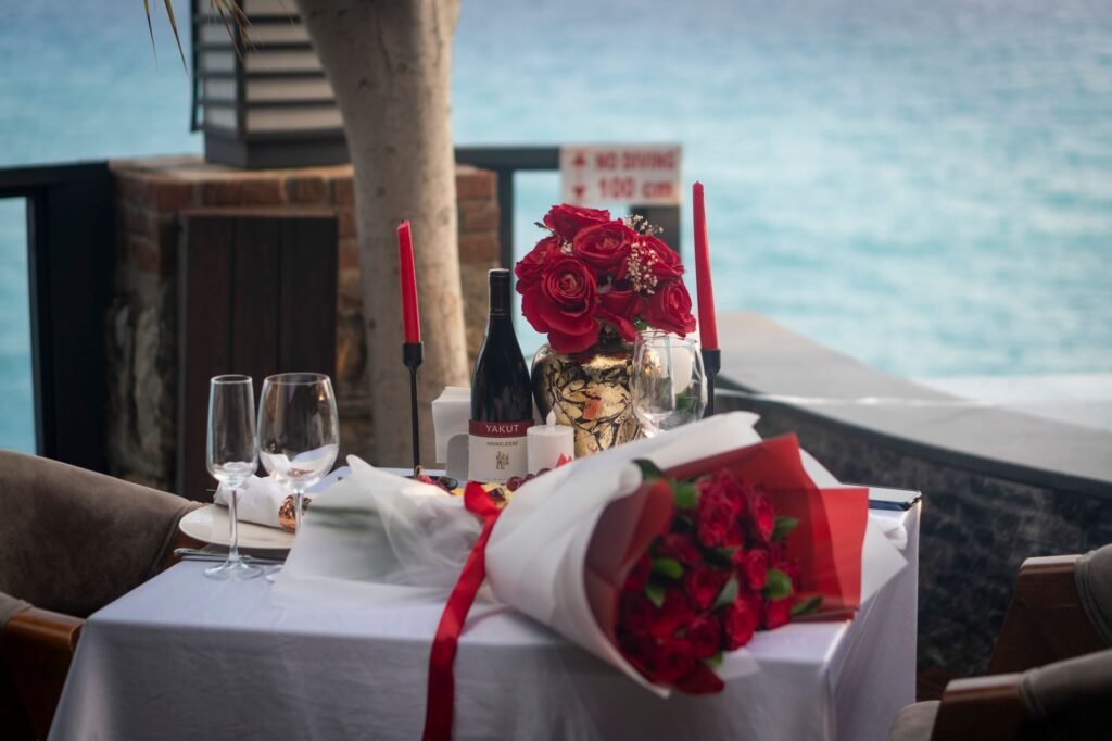 Elegant outdoor dinner setting with red roses and candles by the ocean, perfect for a romantic date.