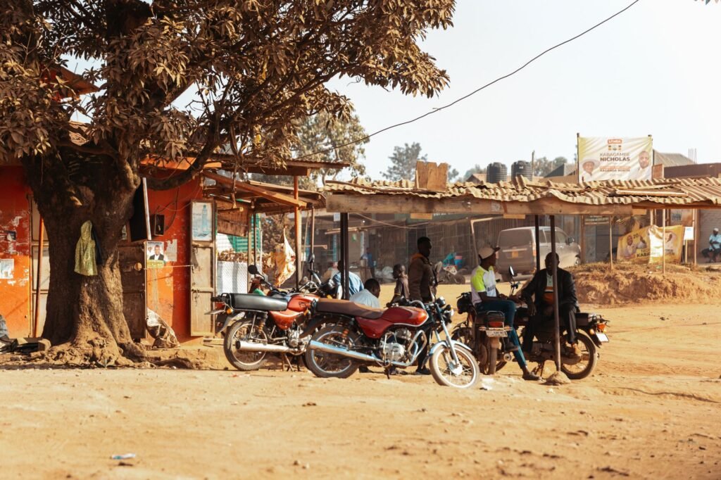 Motorbikes parked under a tree in a Ugandan village, capturing local lifestyle and community.