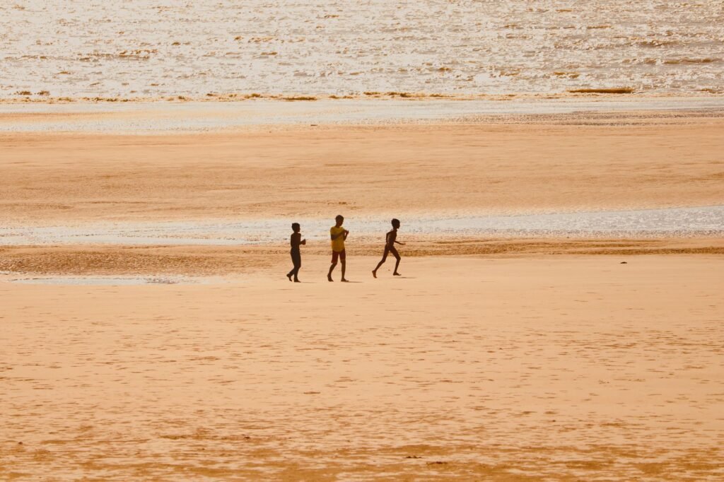 Three children enjoy playing on a vast, sunny beach at low tide, embodying carefree childhood moments.