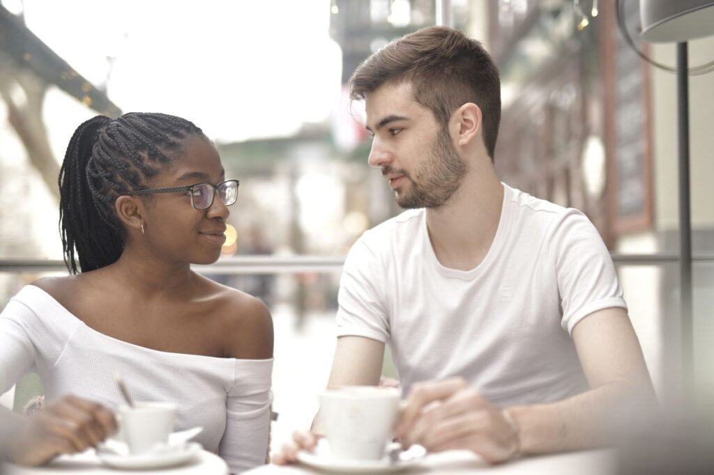 A multiracial couple enjoys coffee together in a bright café setting, sharing a warm moment.