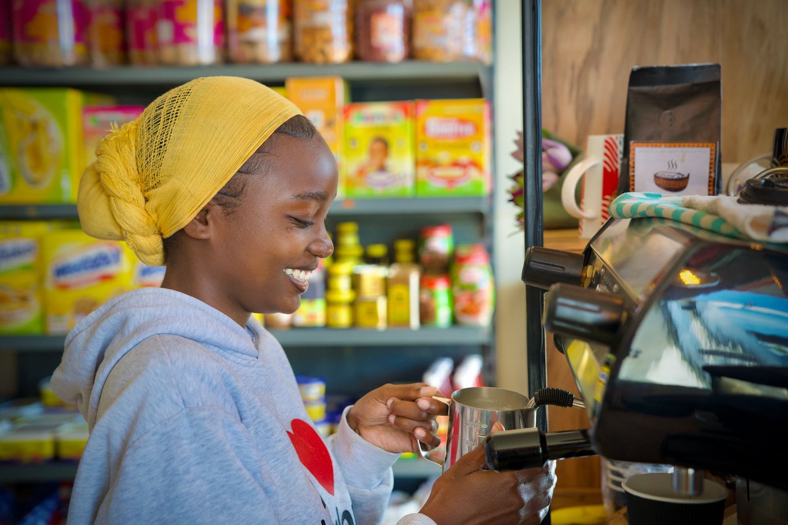 A joyful barista steaming milk in a cozy café with products displayed on shelves, creating a warm ambiance.