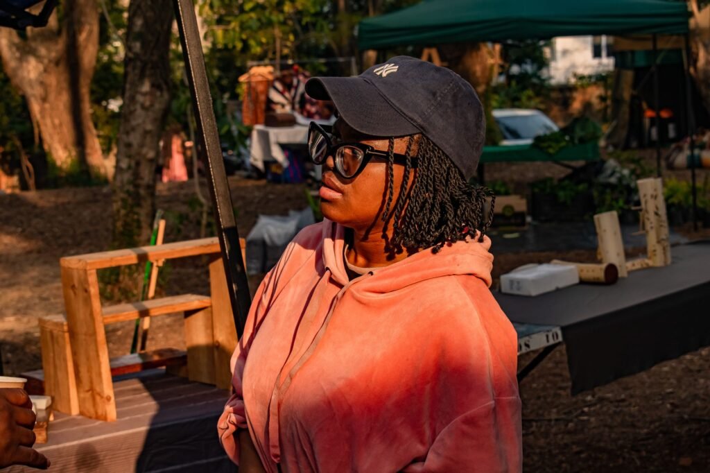 A woman in a pink hoodie and cap at an outdoor market in Malkerns, Eswatini.