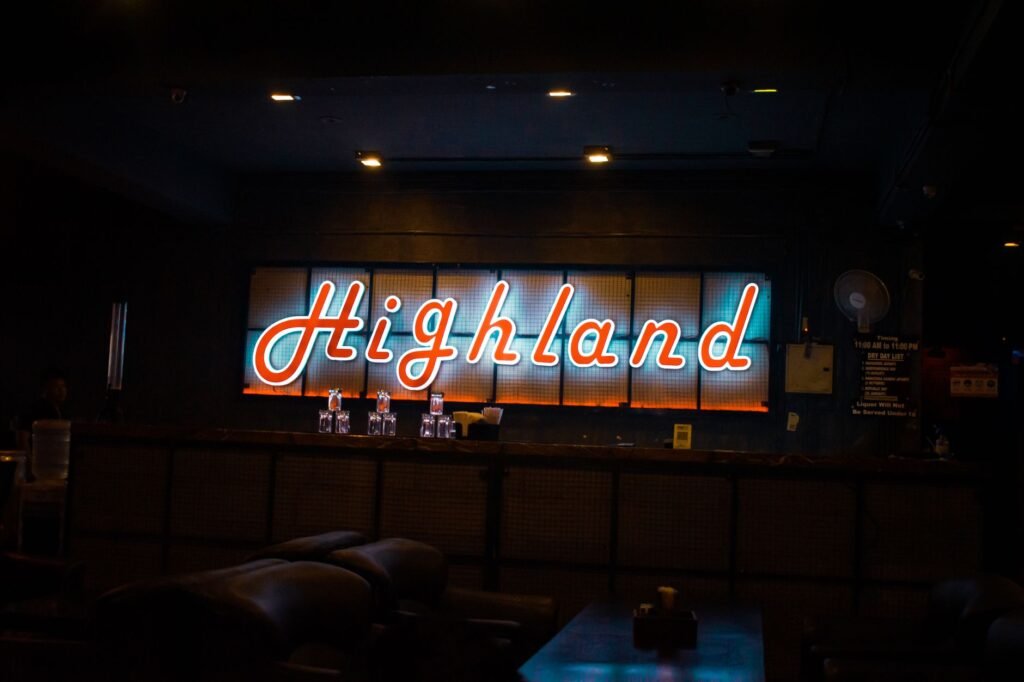 A neon sign reading 'Highland' illuminates a cozy, dark bar interior, creating a vibrant nightlife atmosphere.
