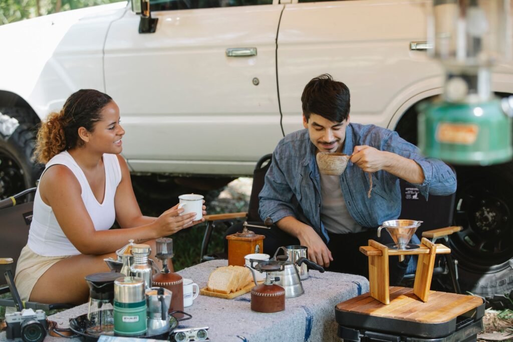 Cheerful multiracial couple in casual summer outfits enjoying aromatic hot pour over coffee during picnic on sunny day