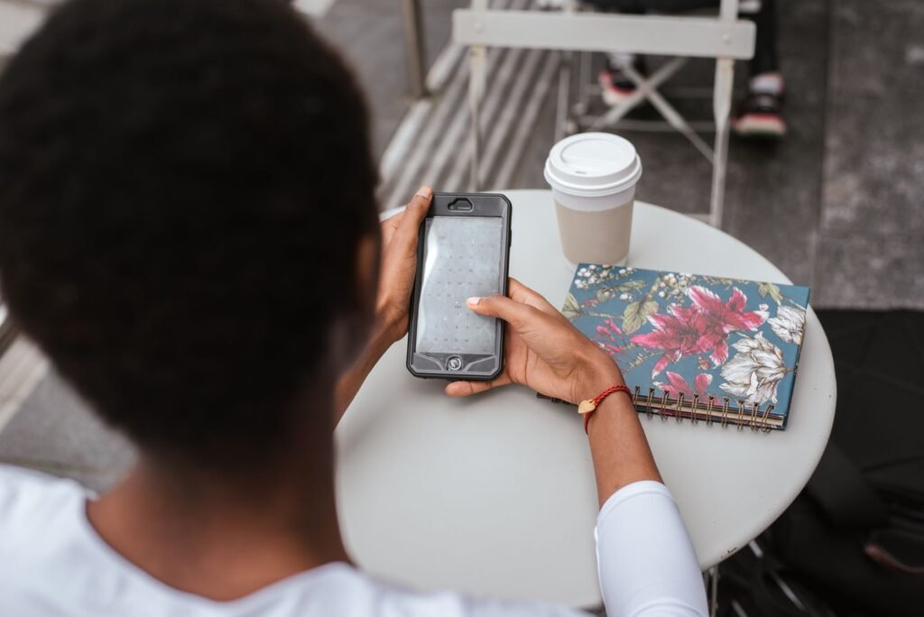 High angle back view of faceless African American lady sitting at table in cafeteria and checking notification on smartphone