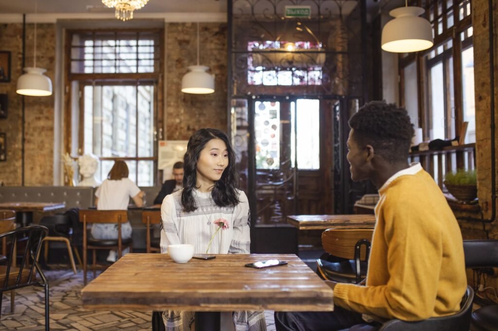 Interracial couple sitting in a cozy cafe, engaged in conversation. Interior design includes rustic elements.