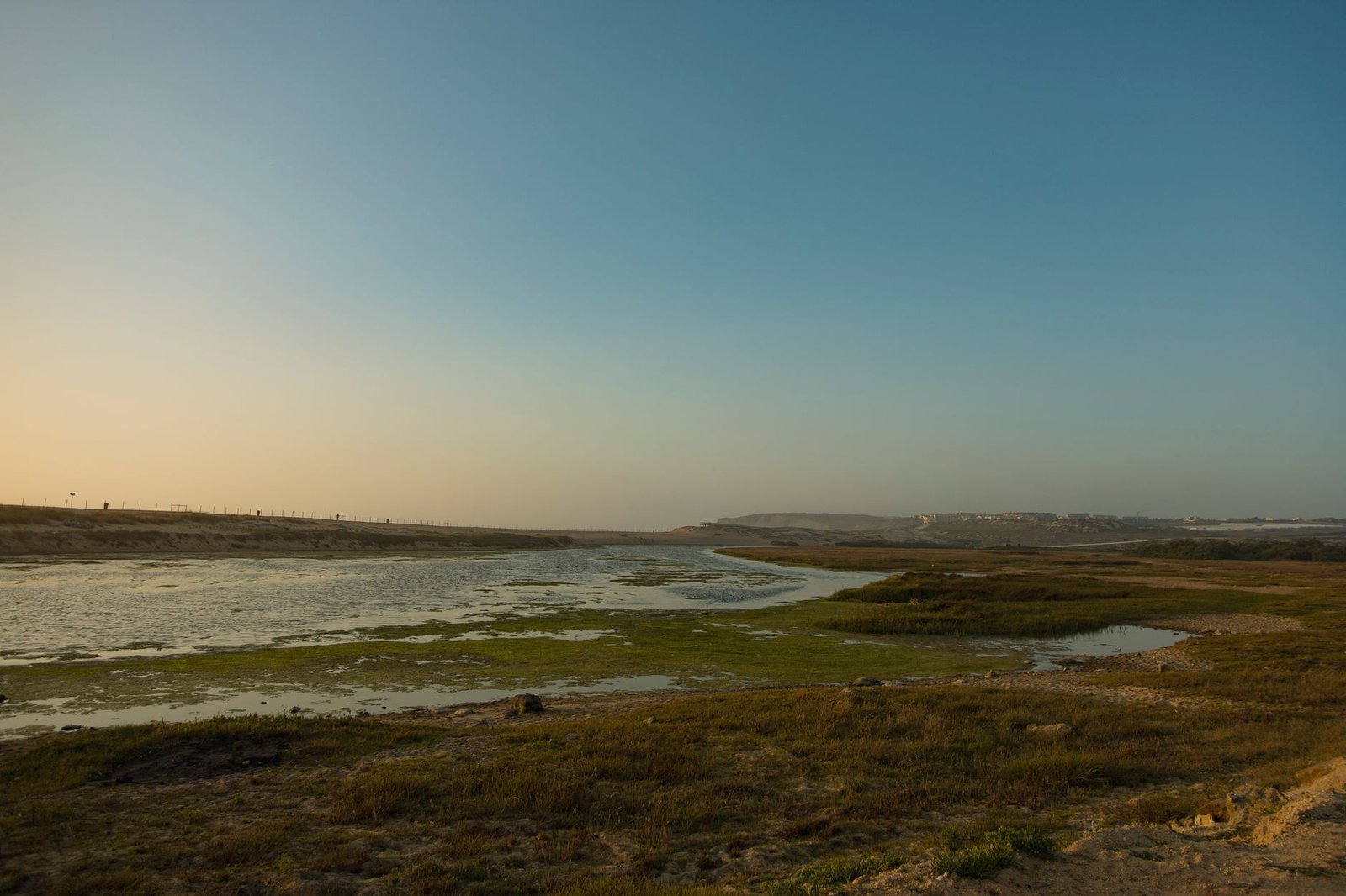 Peaceful view of a coastal landscape with a calm sea and clear sky during sunset.