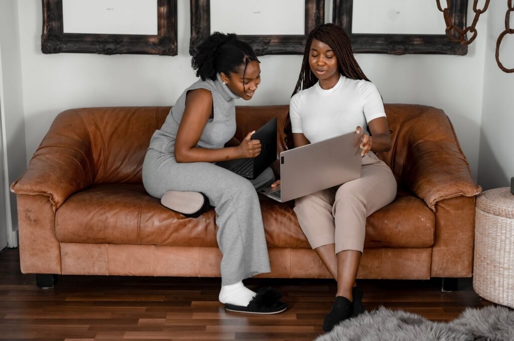 Two African American women working together on laptops in a cozy indoor setting.