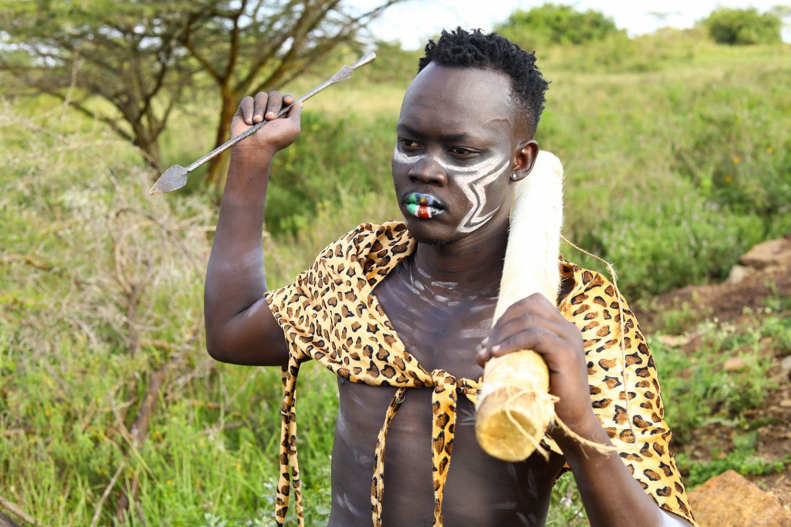 A tribal man in traditional attire with body paint and an arrow in a natural landscape.