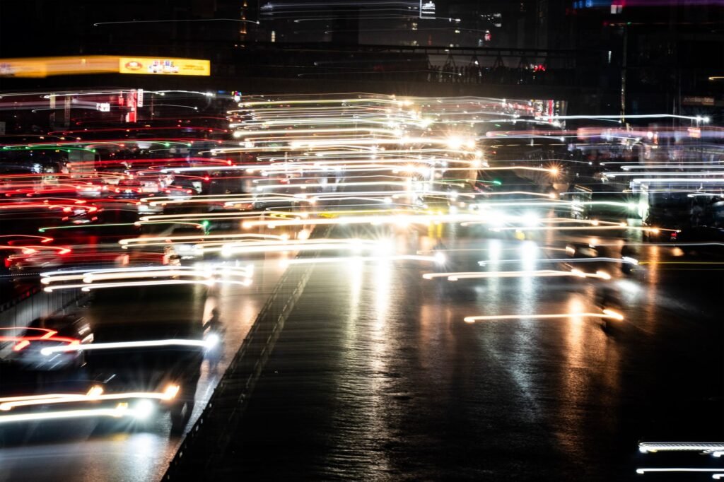 A vibrant city street at night featuring blurred car light trails in motion.