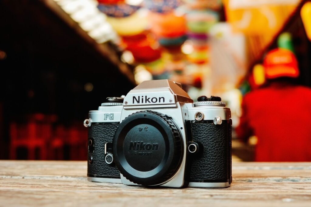 Close-up of a classic Nikon FG film camera on a wooden surface in a colorful indoor market scene.