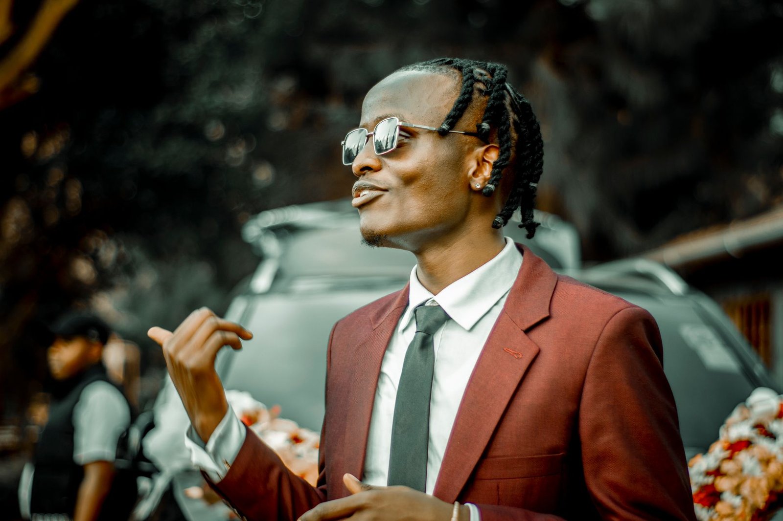 A fashionable man in a burgundy suit with sunglasses at an outdoor event in Nairobi, Kenya.